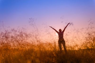 Sunrise scene in a meadow with a person standing with their arms stretching up and out joyfully.