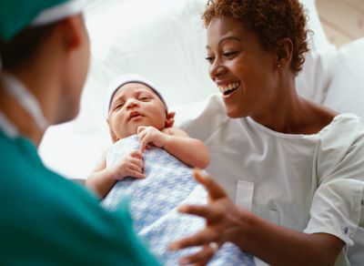 A nurse is handing a newborn infant to a smiling new mother.