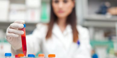 a female scientist in a lab  looking at a pipette full of a red liquid. 