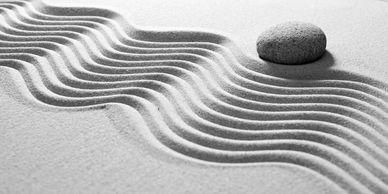 Waves drawn in flat sand with a rake. A smooth stone above the waves.