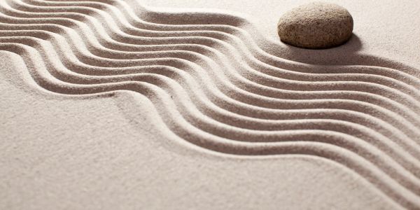 A stone sits beside perfectly drawn ridges in sand.