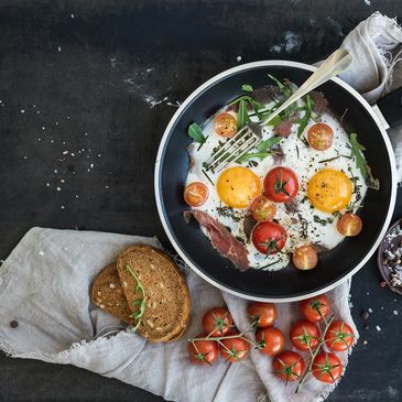 A pan full of sunny side up eggs garnished with herbs and tomatoes.