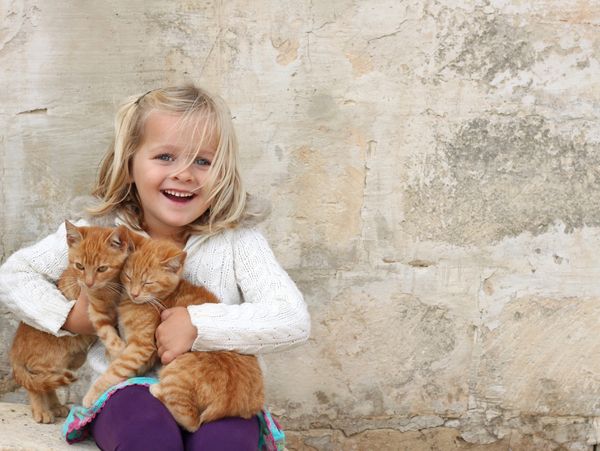 a little girl holding 2 kittens in her arms.