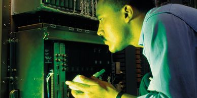 A service technician inspects electrical controls in a dark control panel.