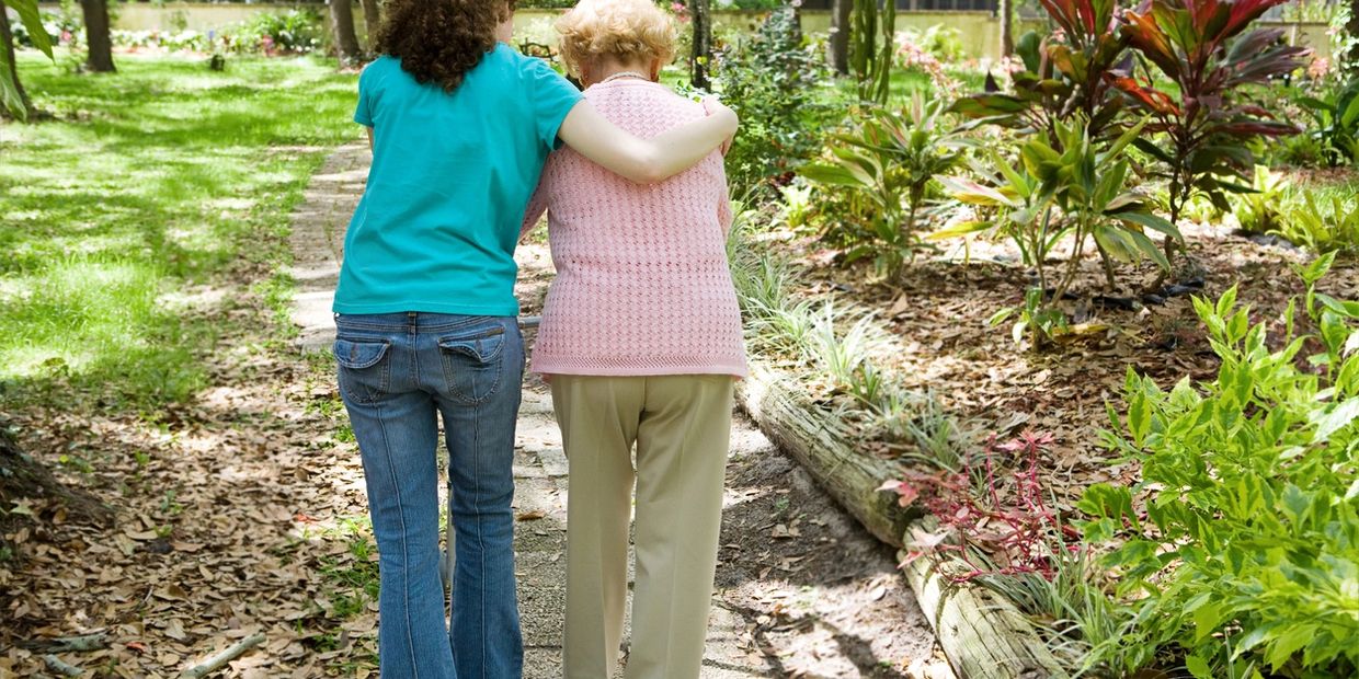 Young woman helping elderly woman walk on path to flower garden
