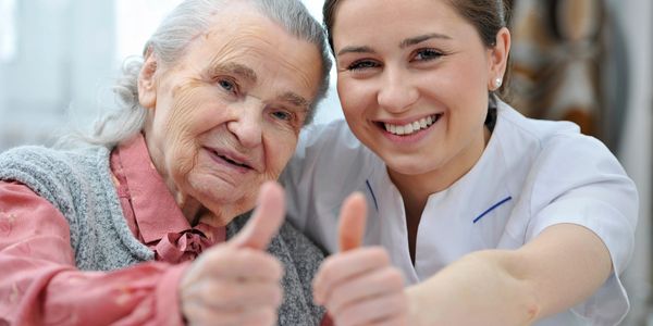 Client and Caregiver hold their thumbs up, smiles on their faces depicting trust between them.
