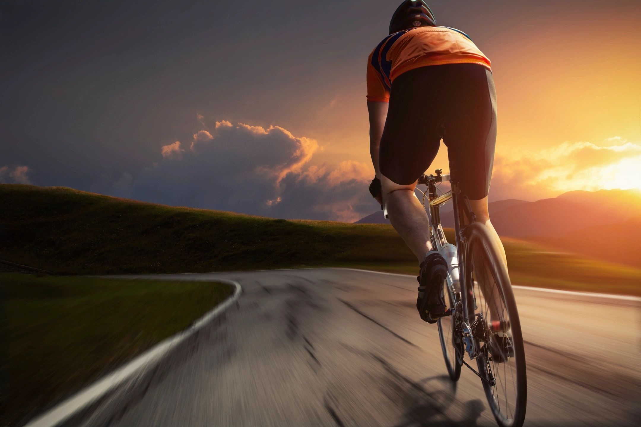 A cyclist on an open road with a colourful sunset in the background