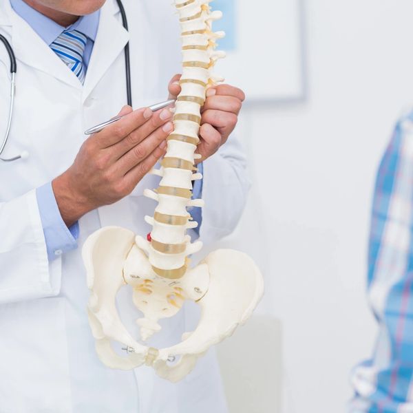A doctor of chiropractic holding a spine and pointing to a vertebrae