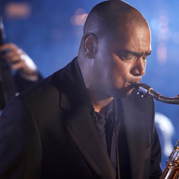 Tenor sax player, blowing his horn as a string bass player is plucking the strings behind him.