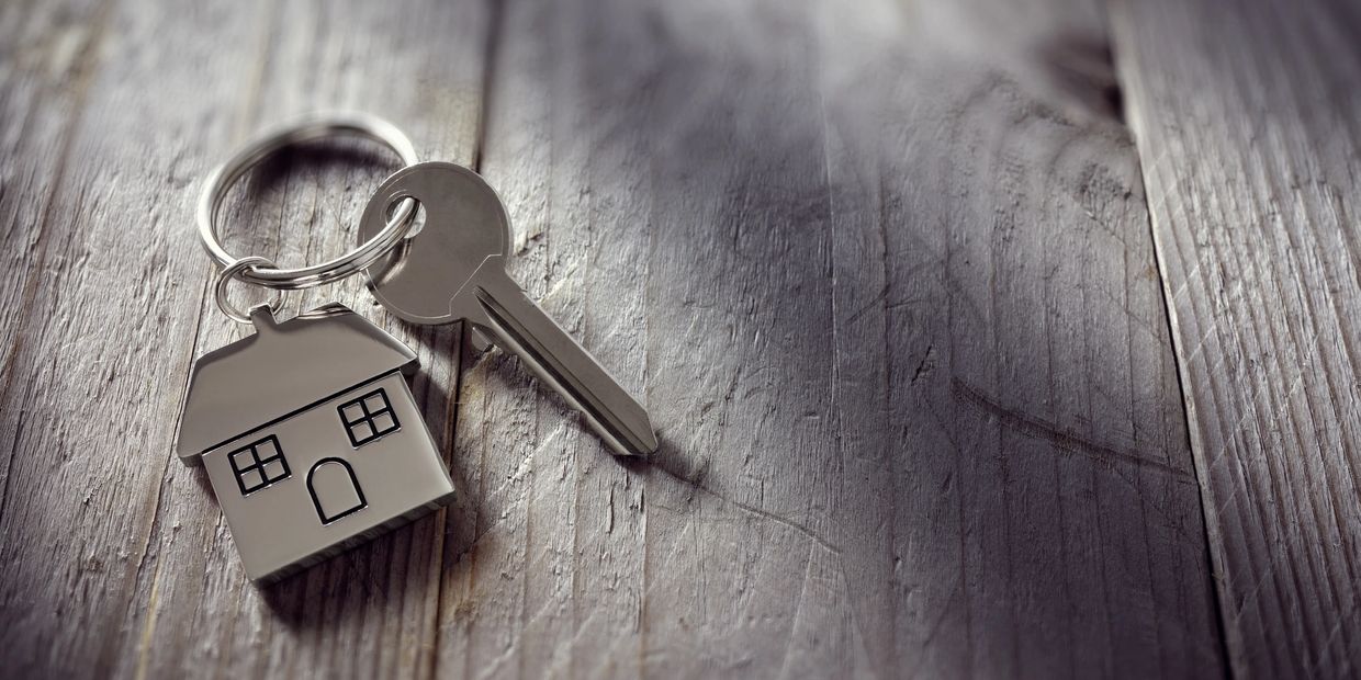 A key chain that looks like a house with one key over a wood background.