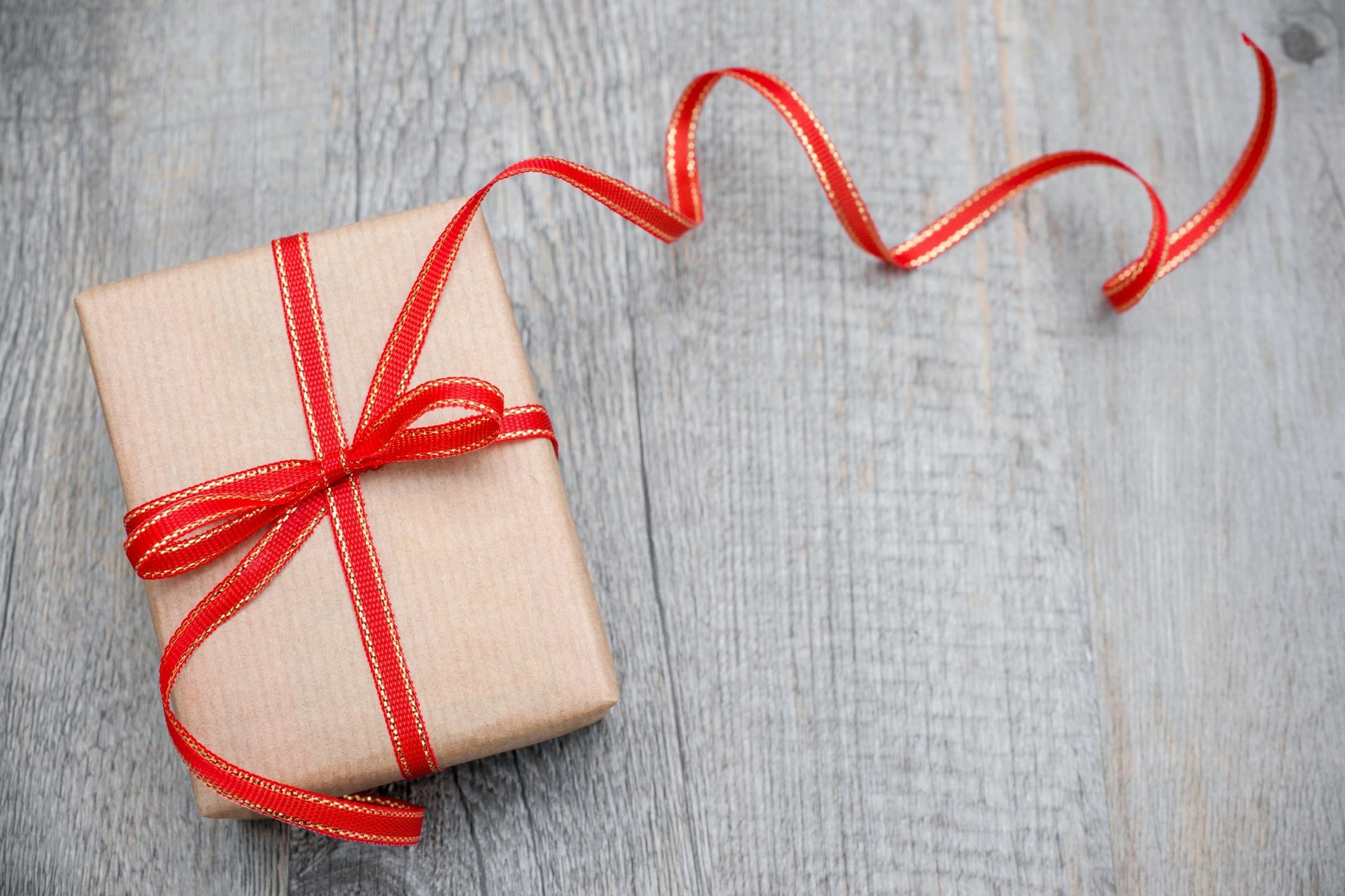 Photo of a gift box wrapped with rustic paper and tied with a red bow.