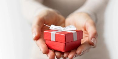 A woman extending her hands holding a small red gift box tied with a white bow.