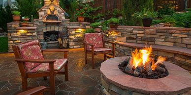 An inviting outdoor seating area with two red cushioned chairs facing a stone fire pit, surrounded b