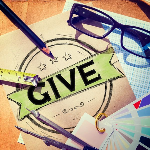 Desktop with glasses, pencil, ruler, and other items with word give for donations. 