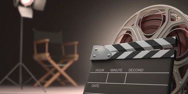 film equipment: Director's chair, set light in background, and film reel with slate in foreground
