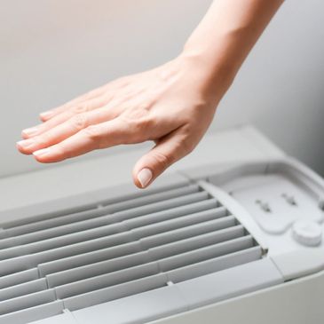 shows a hand over an air conditioner feeling the air temperature
