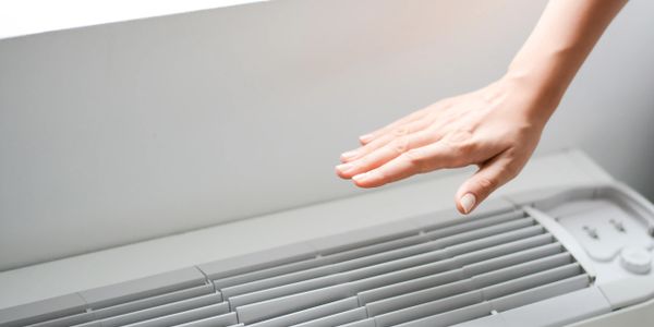 Hand feeling the airflow from a wall air conditioner