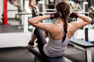Young female in workout room doing sit ups on bench