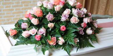 Image of white casket with funeral arrangement of pink and purple and blush roses