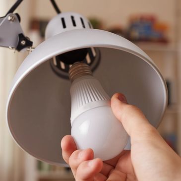 Person's hand adjusting a lightbulb in a white lamp