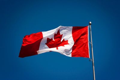 Canadian flag fluttering in the wind in front of a sky-blue background.