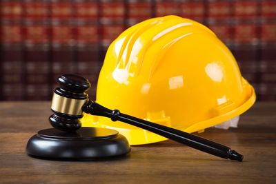 A judicial gavel with a construction hardhat. Law books in the background.