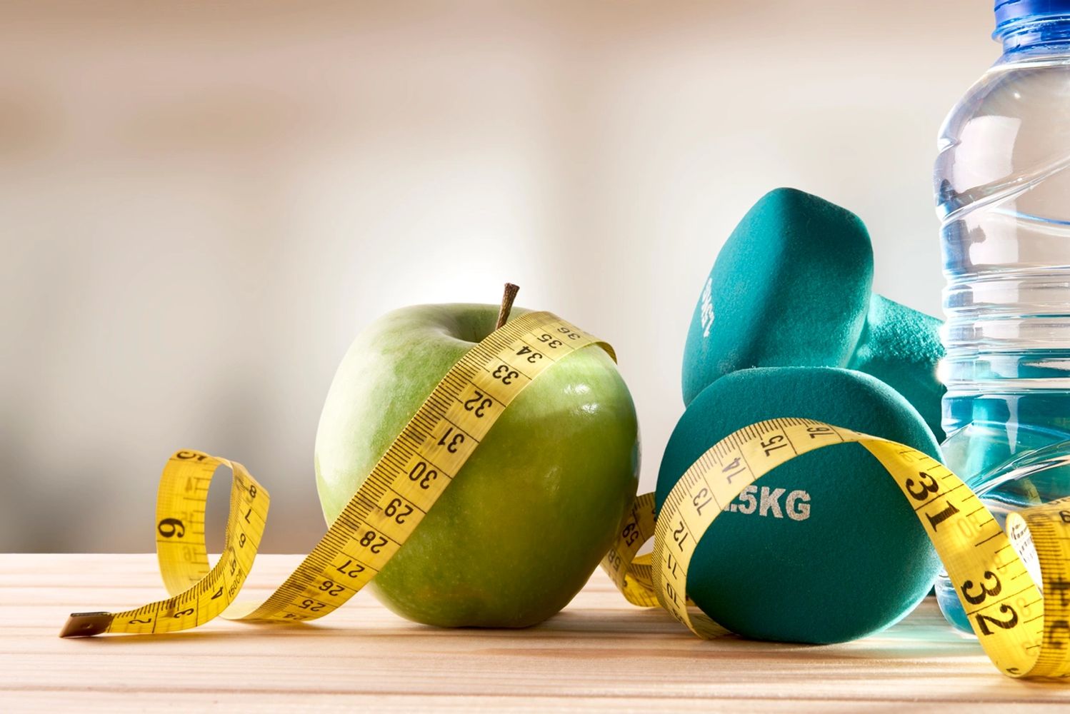 A green apple, hand weights, and a bottle of water with a measuring tape wrapped around them.