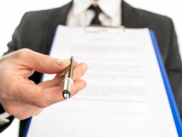 An executive holding a pen out for a signature on a contract.