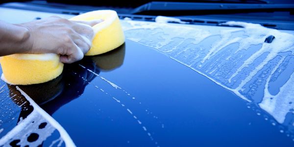 A soapy sponge is swiping the hood of a blue car.