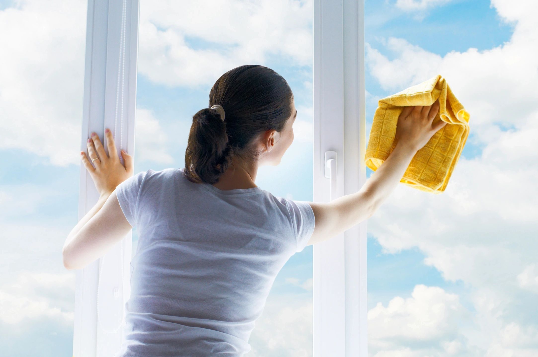 A woman with a rag in her hand cleaning a window.