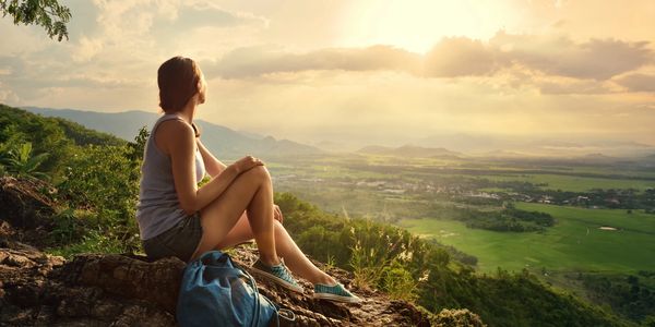 Woman in hiking gear sitting on rocky outlook with sun in background