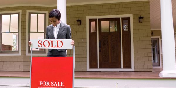 Women placing sold sign in front of home for sale
