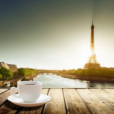 Cup of coffee on wooden dock looking out over river with eiffel tower in the background.