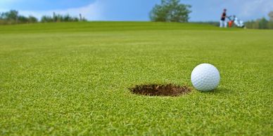Golf ball near hole on green grass