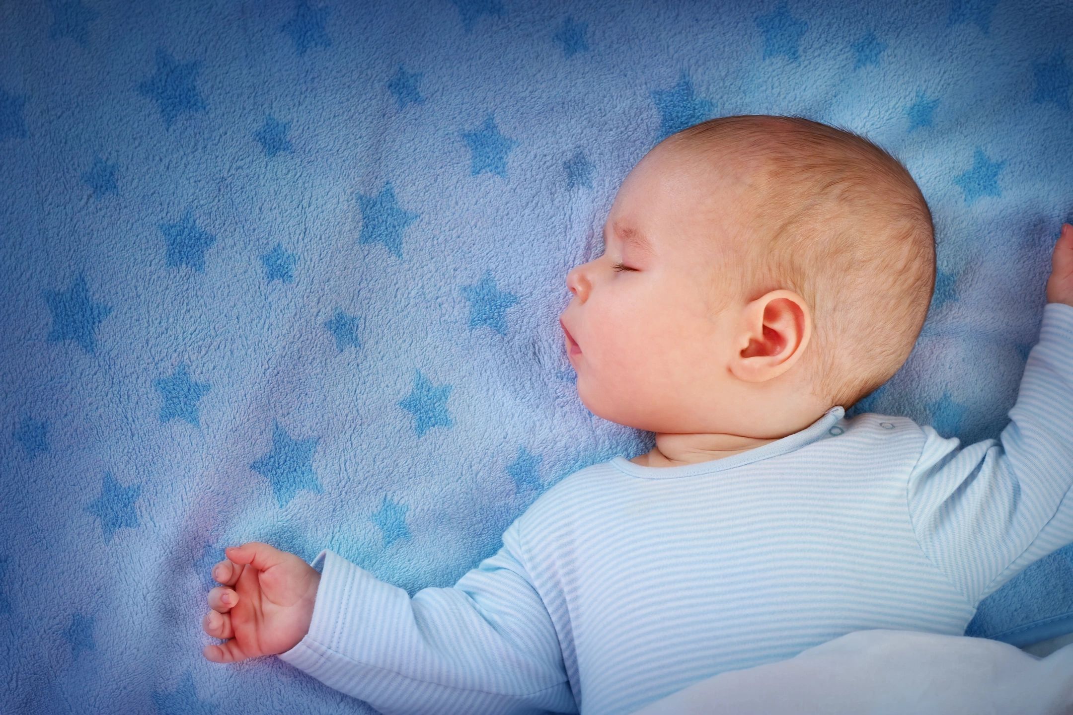 A baby boy asleep on a blue blanket.