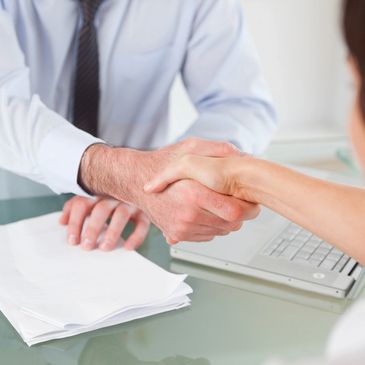 Generic photo of lawyer and client shaking hands with documents on desk below.