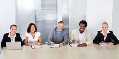 Stock photo of five people sitting at a table with computer and papers in meeting like setting 