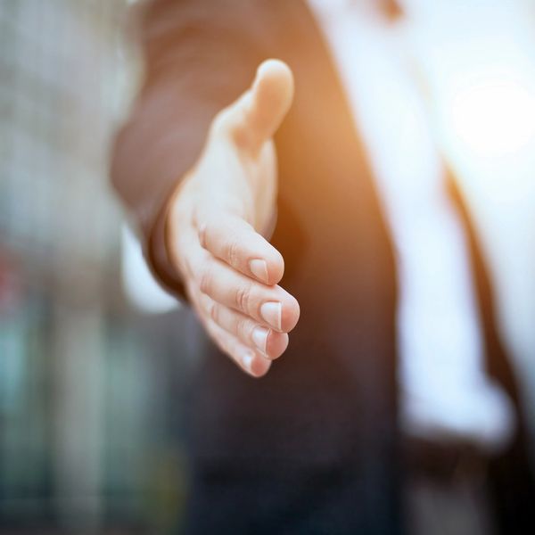 Man holding out hand to offer handshake in front of a business