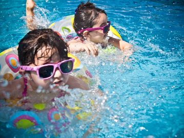 Two young girls swimming in a clean swimming pool on their floaters wearing pink sunglasses