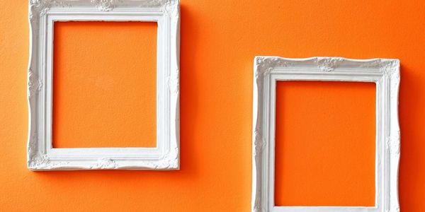 Tap decorative empty white frames placed offset on a bright orange painted wall.