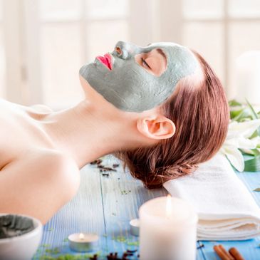 Woman peacefully laying on a table enjoying a mud mask while surrounded bybotanicals and candles.