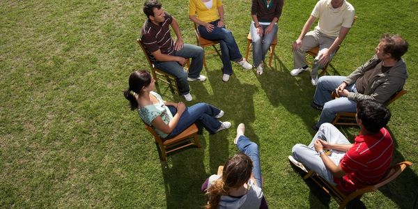 8 People sitting on chairs in a circle outside on the grass. Intuitive Sessions available groups