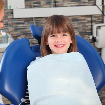 Young girl smiling and sitting in pediatric dental office.
