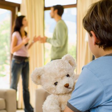 Child holding teddy bear watches parents arguing