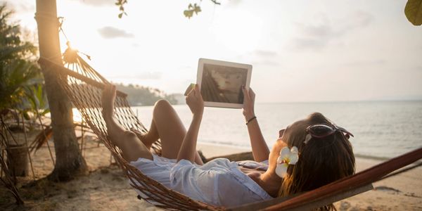 A person using the internet on a tablet while relaxing in a hammock.