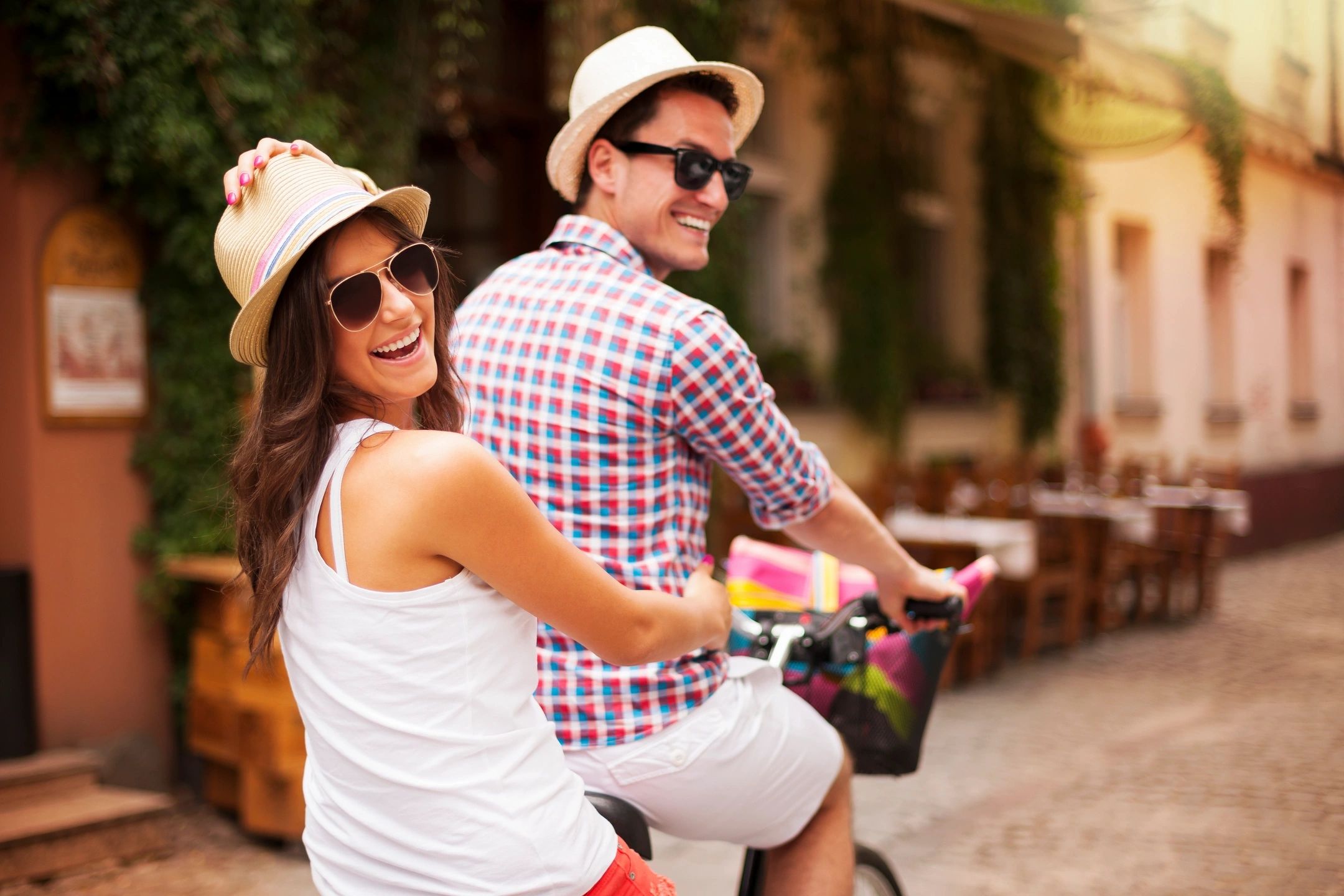 A man and woman smiling while riding a tandem bike past a restaurant 
