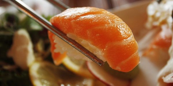 A piece of salmon sushi held by silver chopsticks.