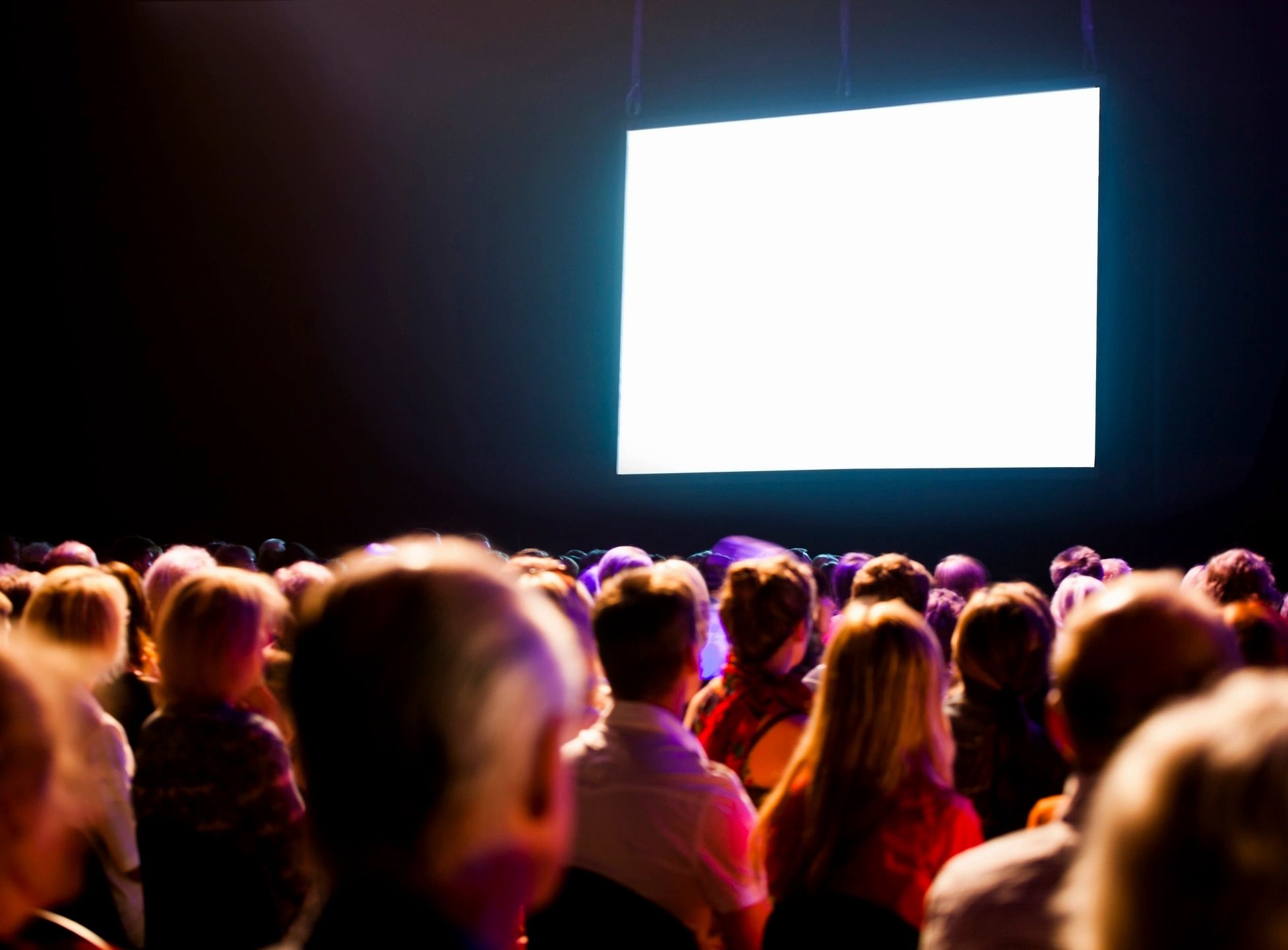 Audience in darkened movie theater looking at bright white screen on the wall