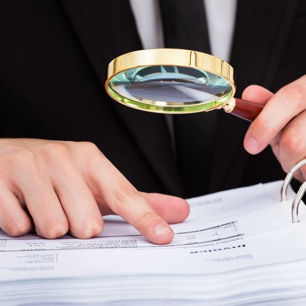 Person with a magnifying glass looking at tax documents 