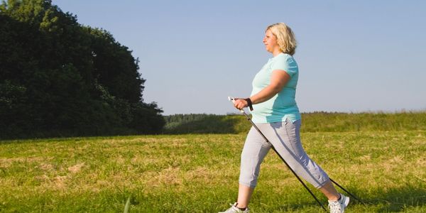 woman overweight walking in the open green field with sticks healthy exercising